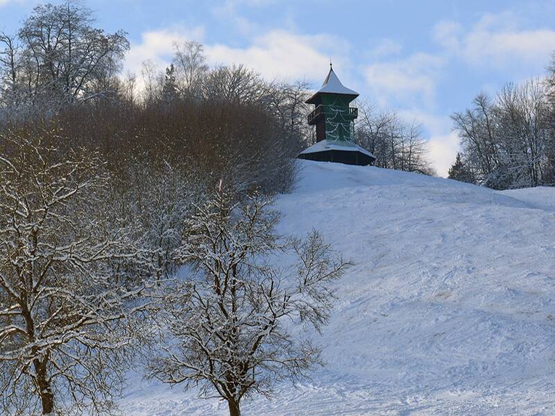 Kernerturm mit Skihang im Winter, rechts und links Gehölze und Bäume ohne Blätter, blauer Himmel mit weißen Wolken