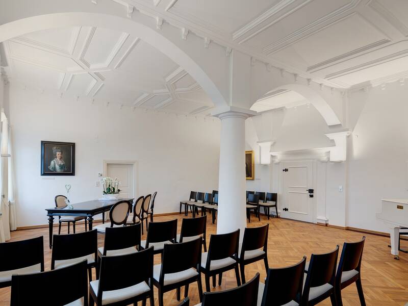 Weißer Saal im Alten Schloss mit schwarzen Stühlen vor weißem gewölbter Decke und Trautisch