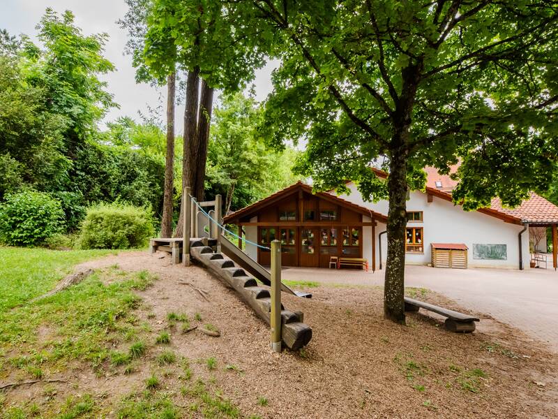 Evangelischer Schlosskindergarten Außenansicht, links vorne ein hölzernes dunkelbraunes Spielgerät